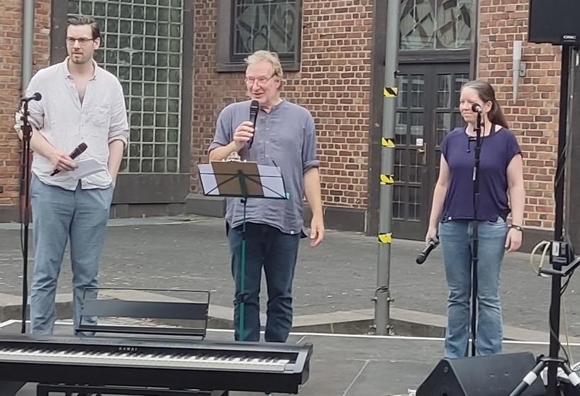 Drei Personen stehen mit Mikros in der Hand im Dinslakener Burginnenhof. Eine Person spricht.
